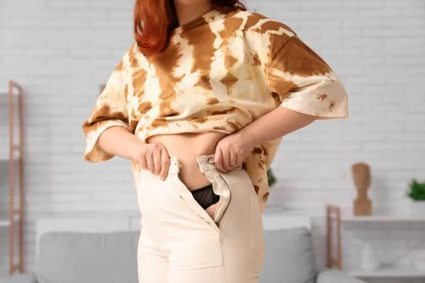 Image of woman trying to do her trousers up after pregnancy weight gain Midhurst