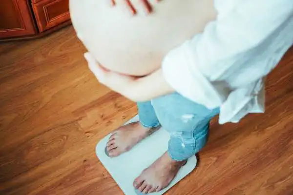 Image of woman weighing herself and experiencing weight gain through pregnancy Midhurst